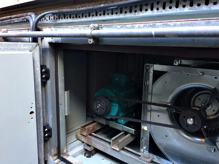 The motor, belts and fan inside an air handling unit with the access panel open
