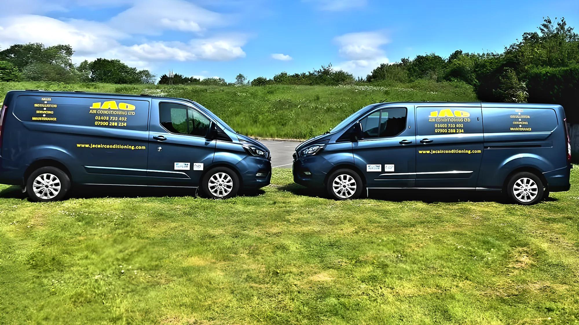 Two JAC Air Conditioning vans parked nose to nose in a field