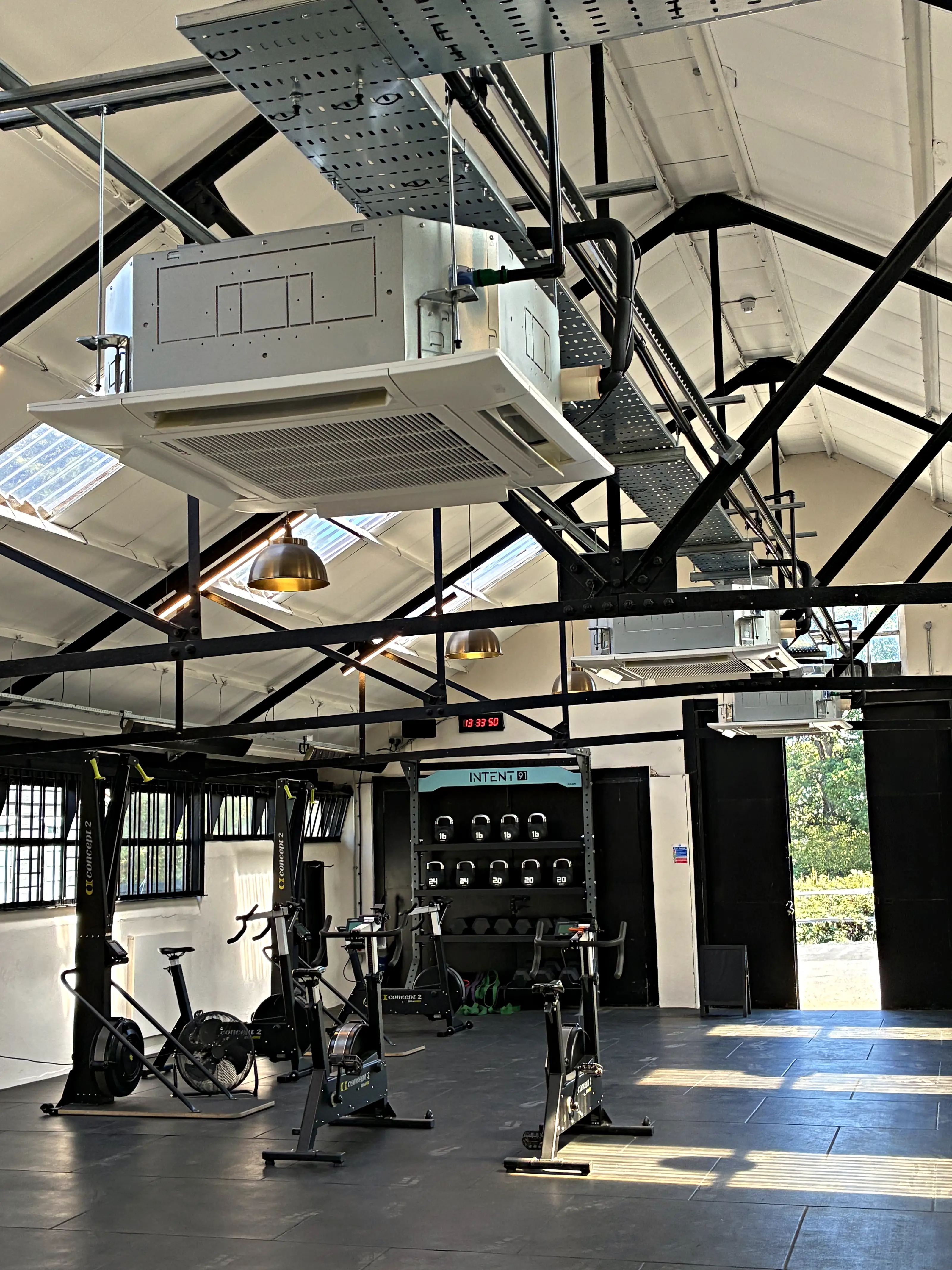 A ceiling cassette above the exercise bikes in a commercial gym with exposed steel trusses