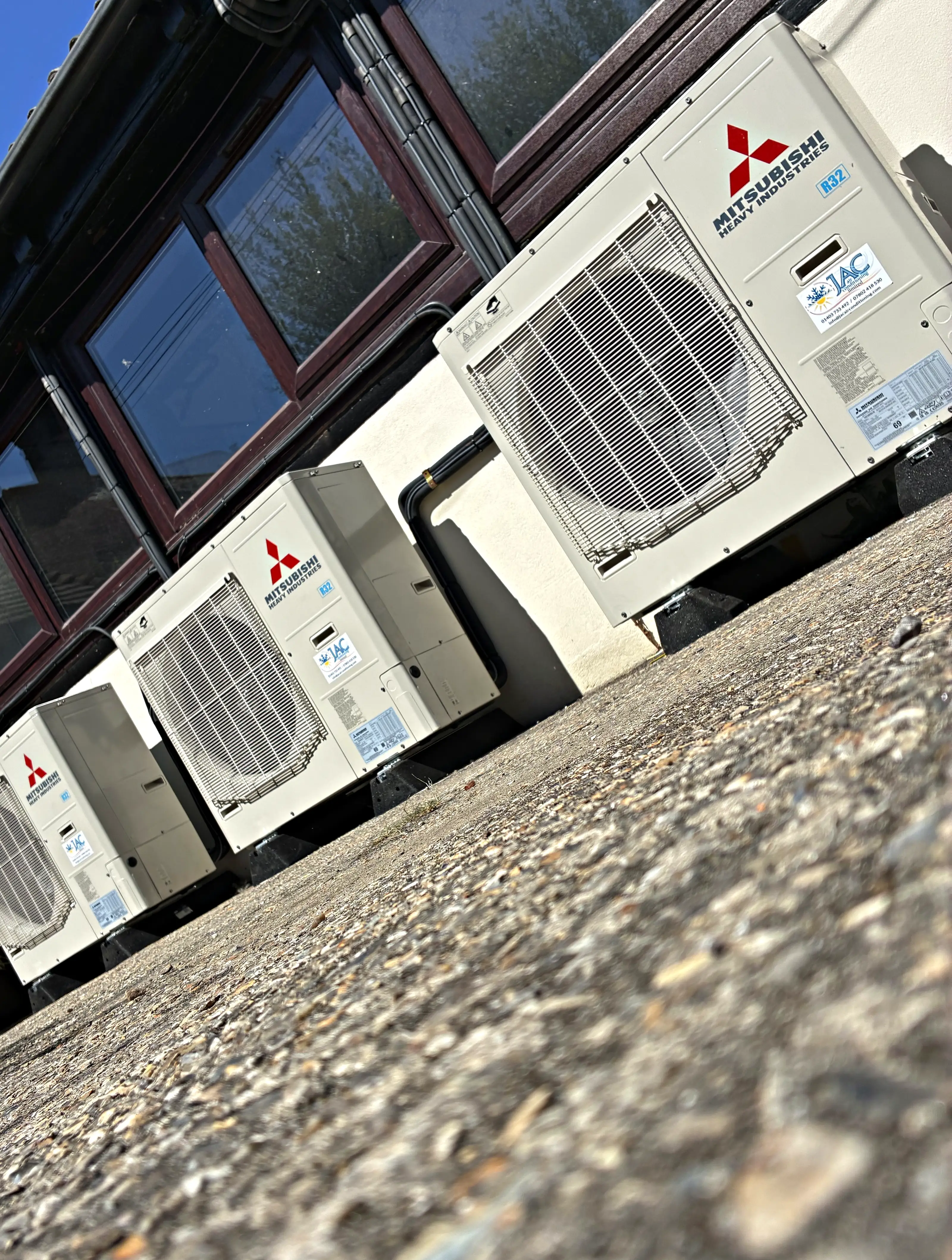 Three Mitsubishi Heavy Industries outdoor units on raised feet along the wall of a commercial gym