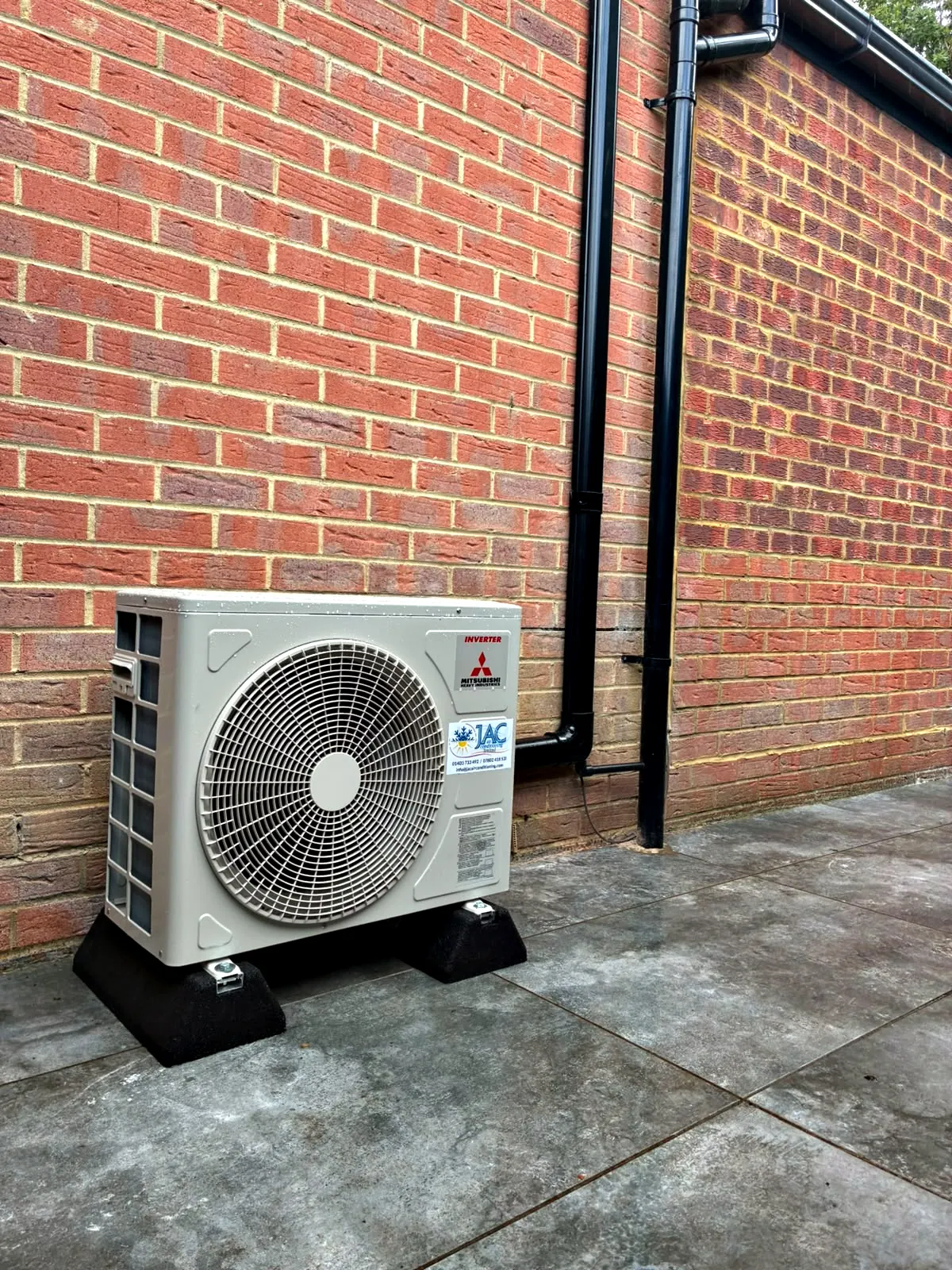 A Mitsubishi Heavy Industries outdoor unit on rubber feet on a paved patio against a red brick wall