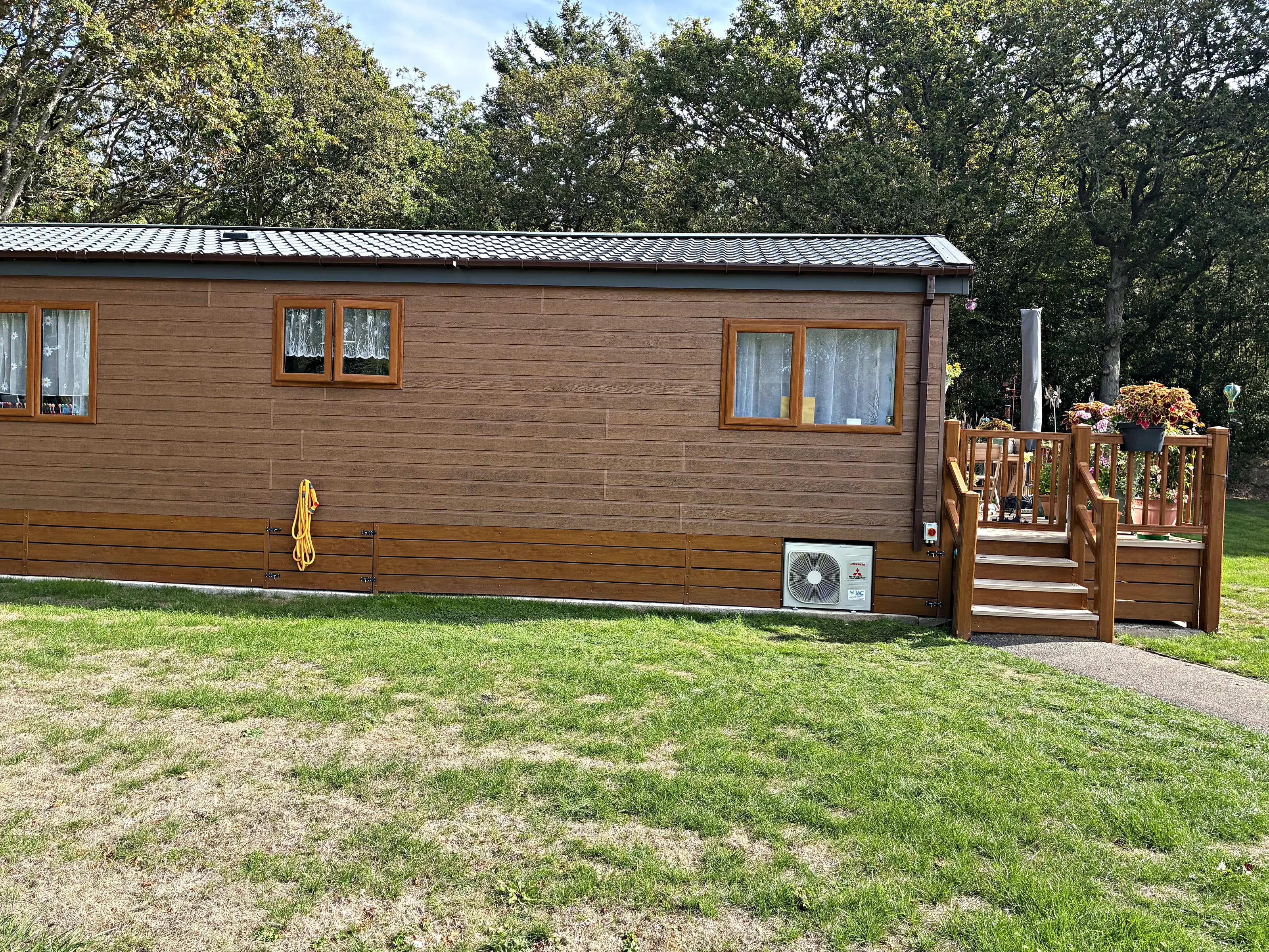 A park home on a lawn with its outdoor unit tucked into the skirting at the far end